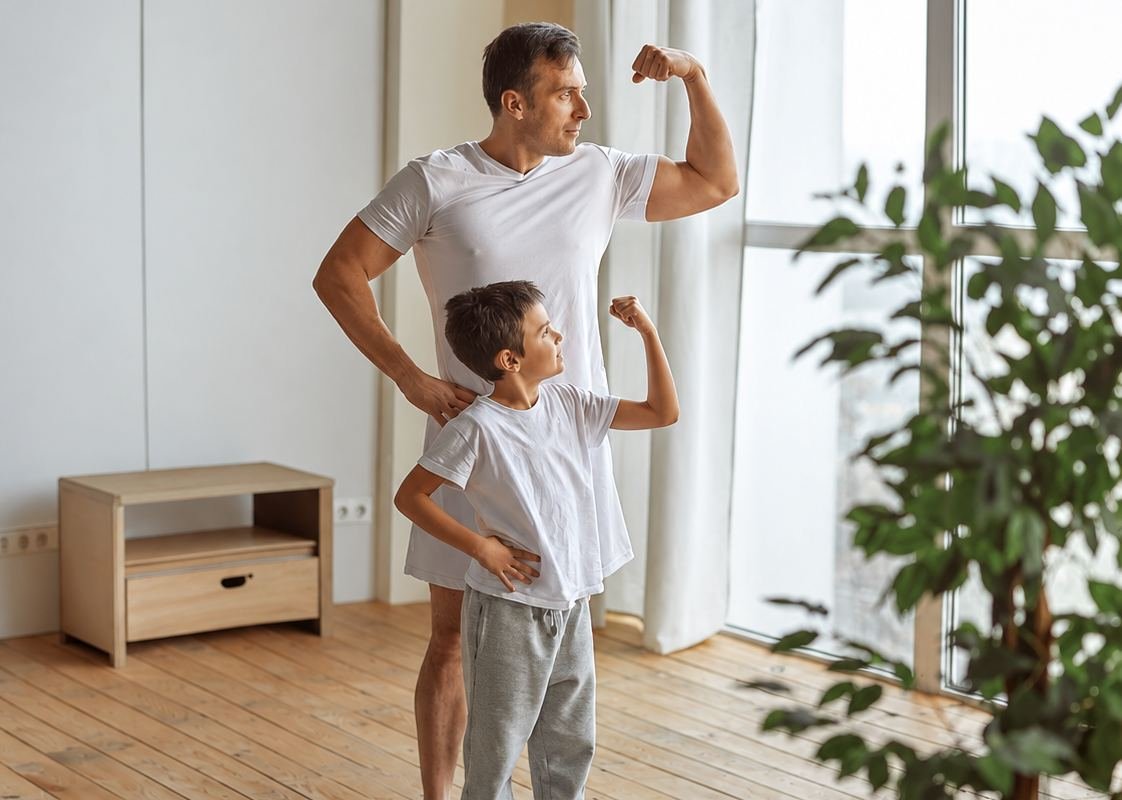 Pai e filho mostrando a força dos braços, em casa